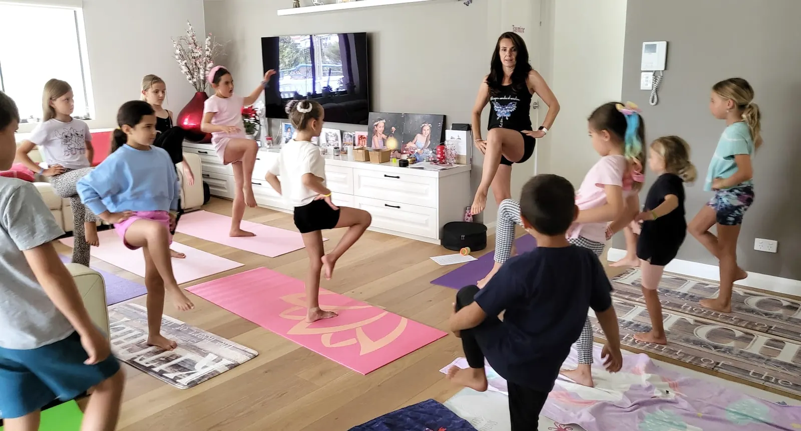 Children of different ages in tree pose together during a Kids For Yoga session